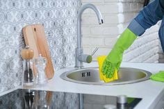 a person in green gloves cleaning a kitchen sink with a yellow sponge on the edge