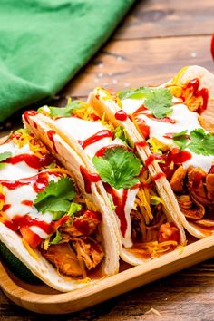 three tacos on a wooden tray with sauce and cilantro