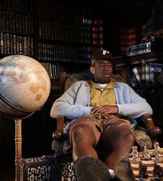 a man sitting in a chair next to a giant globe and chess set on top of a table