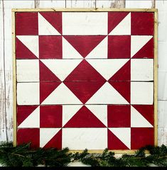 a red and white wall hanging on the side of a building with pine branches in front of it