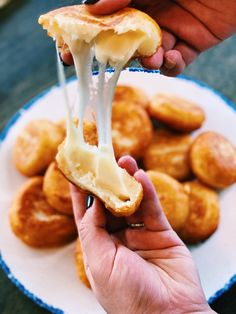 a person holding a piece of bread with cheese on it and dipping sauce over them