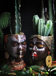 two african masks are sitting next to each other in front of cacti and succulents