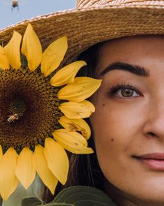 a woman wearing a straw hat with a sunflower in front of her face and bees on the background