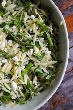 a white bowl filled with pasta and asparagus on top of a wooden table