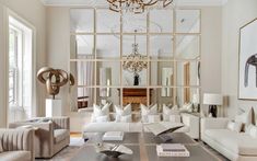 a living room filled with lots of white furniture and mirrors on the wall above it