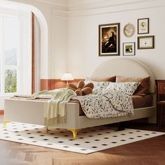 a bed sitting on top of a hard wood floor next to a white wall with pictures above it