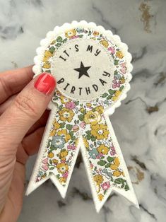 a hand holding a flowered ribbon with the words it's my birthday on it