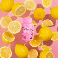 a bottle of women's multi vitamin pill surrounded by lemons on a pink background