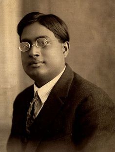 a black and white photo of a man wearing glasses with a suit jacket and tie