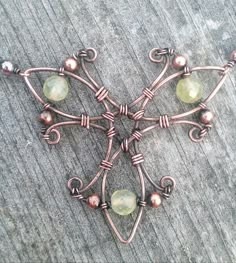 a cross made out of copper wire with green beads on the sides and brown glass bead around it