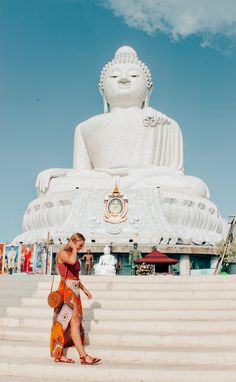 a woman is walking down some steps in front of a large buddha statue