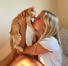 a woman sitting on a bed kissing a cat