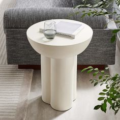 a white table with a book and glass on it next to a couch in a living room