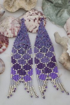 purple and white beaded earrings on shells with seashells in the back ground