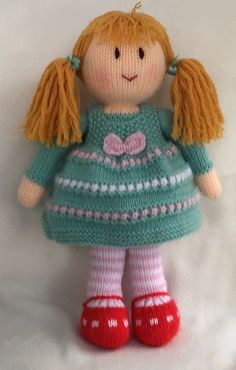 a knitted doll with blonde hair wearing a green dress and red shoes on a white background