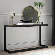 a black console table with a mirror and candles on it next to a white rug