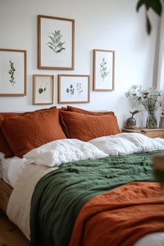 a bed with orange and green blankets in a bedroom next to pictures on the wall