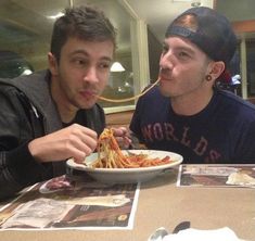 two men sitting at a table eating spaghetti with chopsticks in front of them