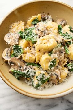 a bowl filled with pasta and mushrooms on top of a marble countertop next to a fork