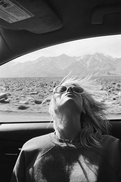 a woman sitting in the back seat of a car looking up at mountains and sky