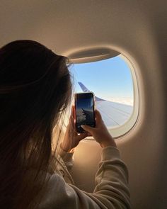 a woman is looking out an airplane window at the wing and taking a photo with her cell phone