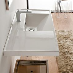 a white bathroom sink sitting on top of a wooden floor next to a mirror and rug