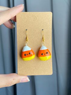 a pair of yellow and orange earrings with black eyes on them, hanging from a card