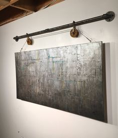 an abstract painting hangs on the wall next to two metal pipe holders with hooks hanging from them