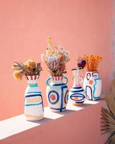 three vases with flowers in them sitting on a ledge next to a pink wall