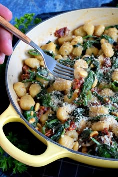 a person holding a fork in a skillet filled with pasta and spinach