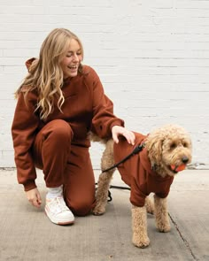 a woman is petting a dog wearing a brown outfit and white tennis shoes while sitting on the ground