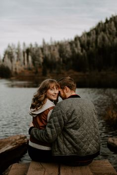 a man and woman are sitting on a dock by the water looking at each other