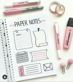 a notebook with paper notes and pink pens on it next to some other office supplies