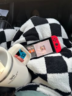 a person holding a nintendo wii game controller next to a coffee cup on a blanket