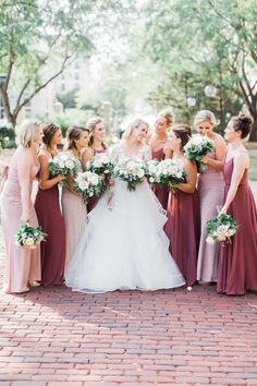 a group of women standing next to each other in front of trees and flowers on a brick floor