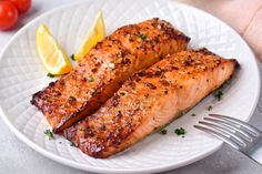 two salmon fillets on a white plate with lemon wedges