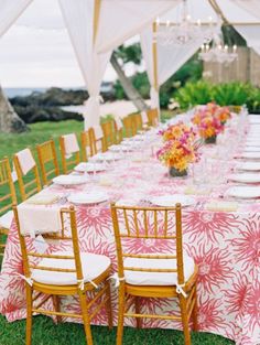 a long table is set with pink and white linens for an outdoor wedding reception