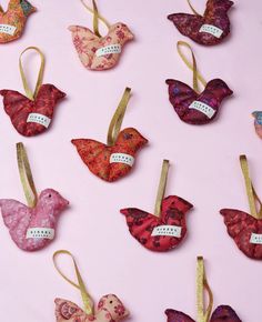 many different ornaments are hanging on a pink surface with gold ribbons and tags in the shape of birds