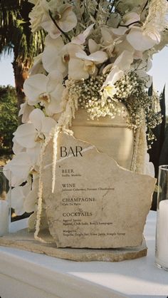 a table topped with a vase filled with white flowers next to a sign that says bar