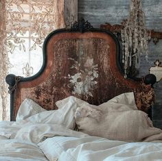 an old wooden headboard with white linens and pillows on a bed in front of a window