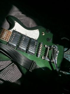 a green electric guitar laying on top of a bed next to a pair of scissors