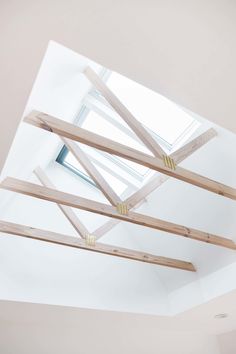 an unfinished ceiling with wooden beams and skylight in the center, on top of a white wall