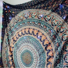 an intricately designed tapestry hanging on the wall in front of a white wall with lights