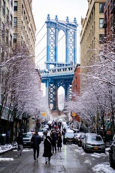 people walking down a snowy street in front of tall buildings with a bridge above them