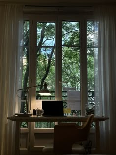 a laptop computer sitting on top of a wooden desk in front of a large window