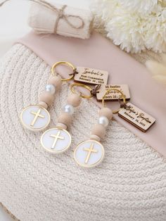 three key chains with crosses on them sitting next to a white pillow and flower bouquet