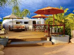 an airstream is set up on a deck with umbrellas and potted plants