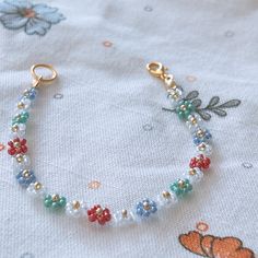 the beaded bracelet is sitting on top of a white sheet with flowers and leaves