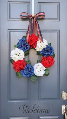 a wreath with red, white and blue flowers is hanging on the front door to welcome people