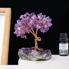 a small purple tree sitting on top of a rock next to a bottle of essential oils